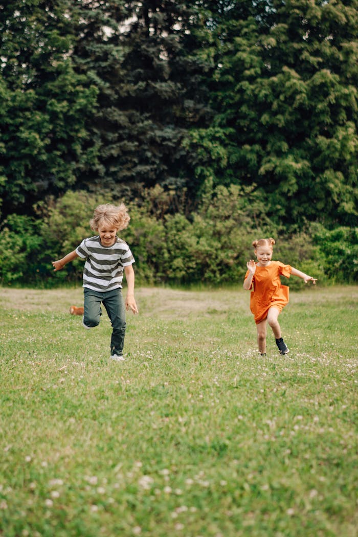 Home Two happy children joyfully running on a sunny day in a lush green field, enjoying outdoor fun.